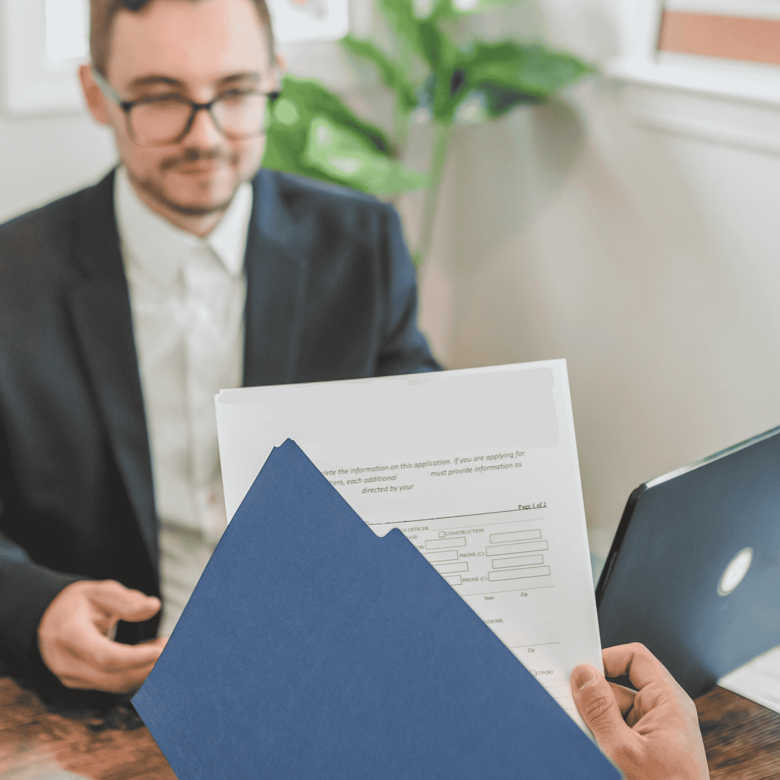 business licensing photo A person hands a business document in a blue folder to a man in a suit during a professional meeting.