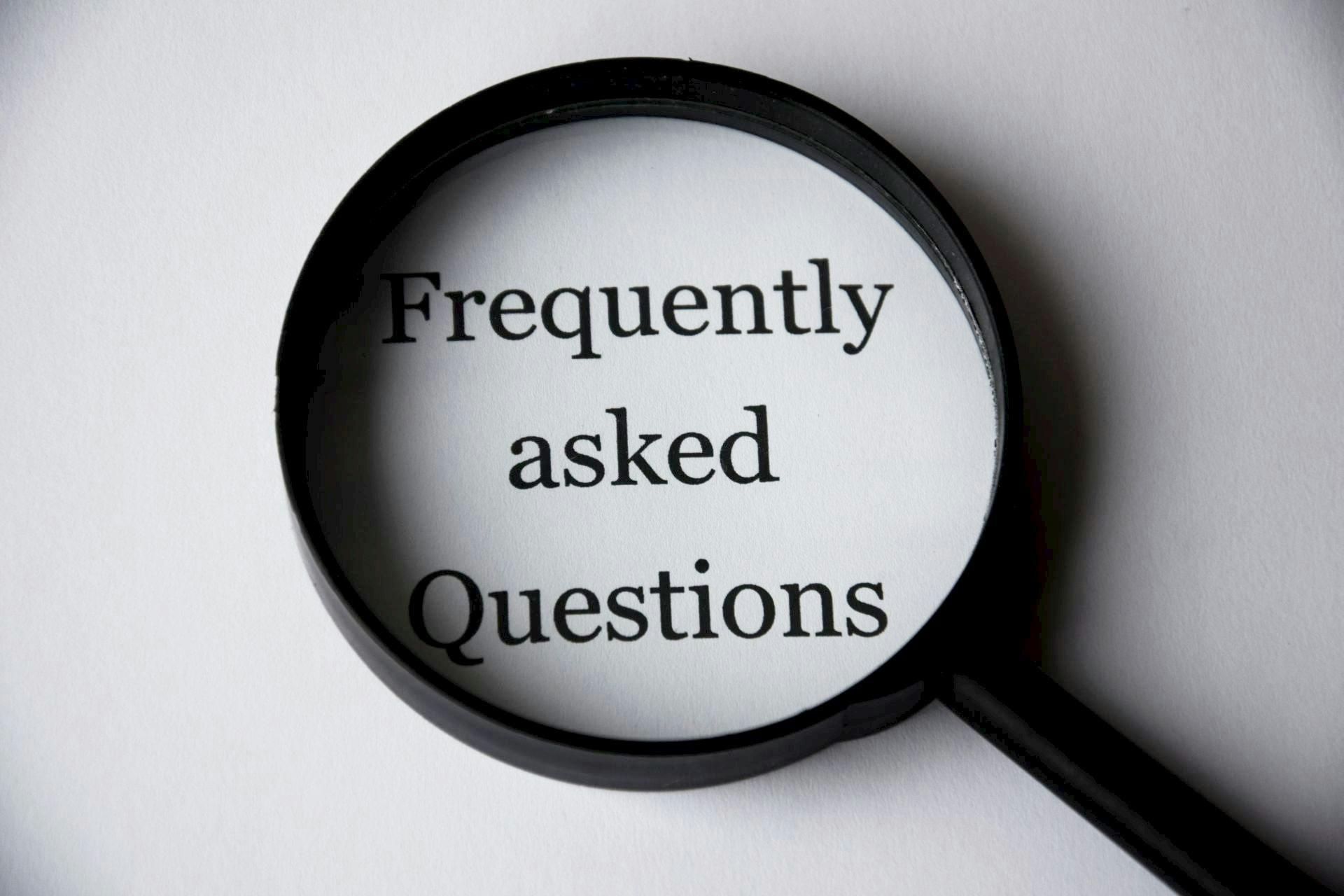 FAQ A magnifying glass highlighting the words "Frequently asked Questions" on a white background.